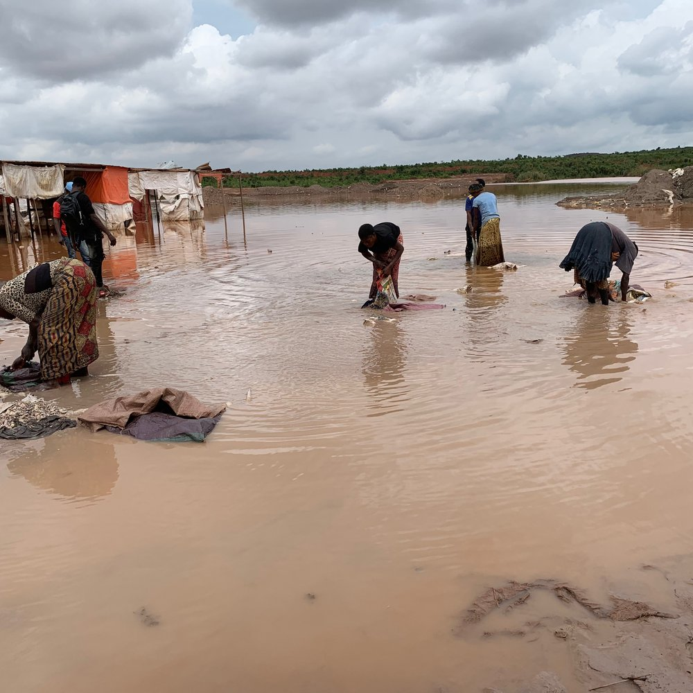 Women washing clothes in muddy water near makeshift shelters in a mining-affected community in the DRC